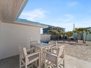 Una veranda con tavolo e sedie, una zona coperta e vista su una casa con balcone e palme.