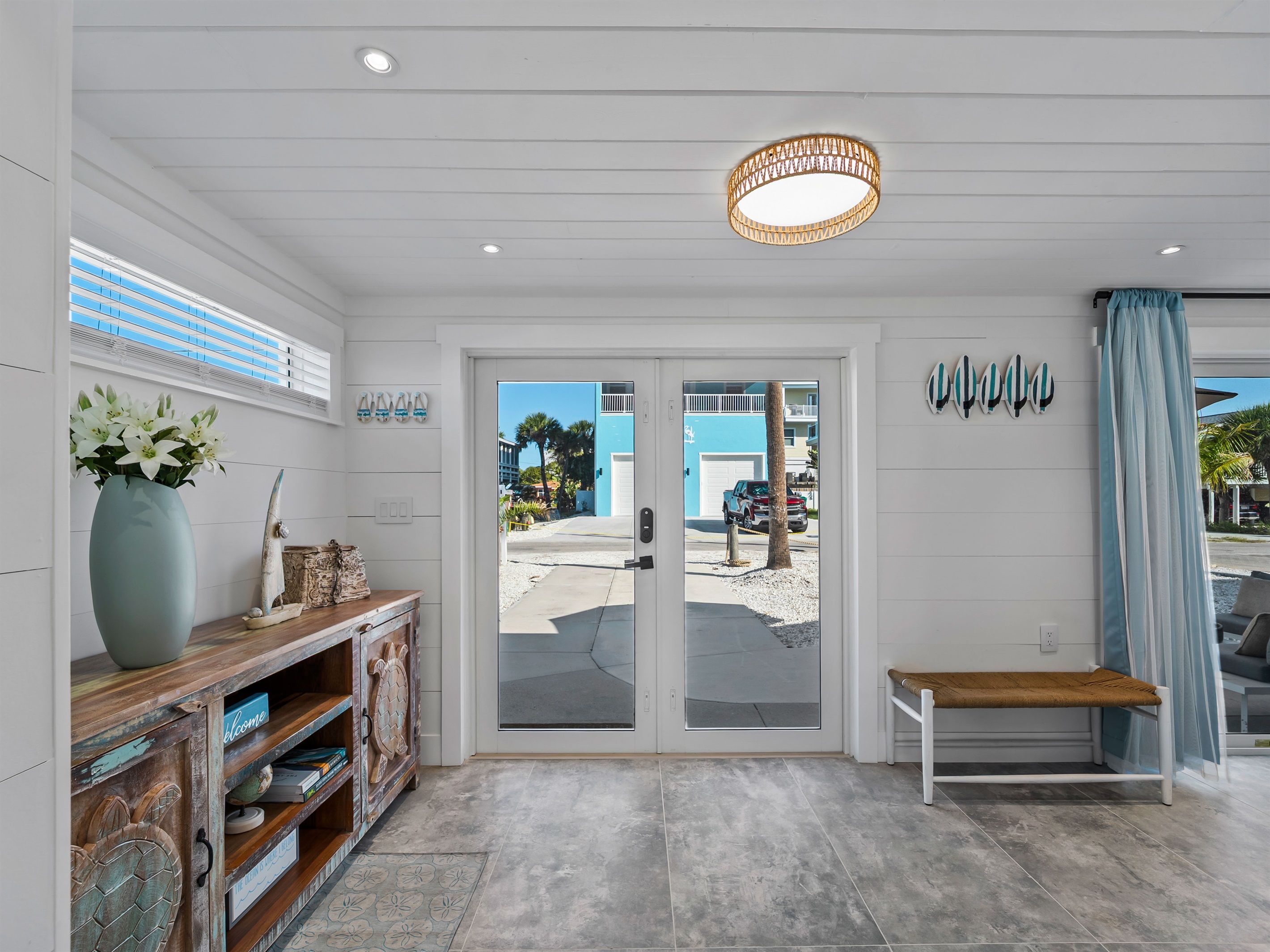 Een modern interieur met een bank, een deur die naar buiten leidt, en een muur versierd met surfboard afbeeldingen.