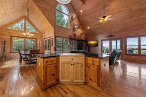 A spacious wooden cabin with a large kitchen island, dining area, and multiple windows offering scenic views.