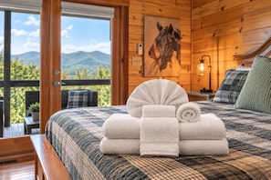 Une chambre d’hôtel avec un lit, un tableau représentant un cheval et une vue sur les montagnes par la fenêtre.