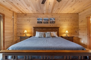 Ein Schlafzimmer einer Holzhütte mit einem großen Bett, zwei Nachttischen mit Lampen und einem Deckenventilator.