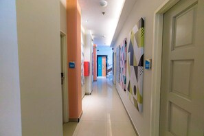 Pasillo de hotel con puertas numeradas, una puerta azul a lo lejos y coloridas obras de arte en las paredes.