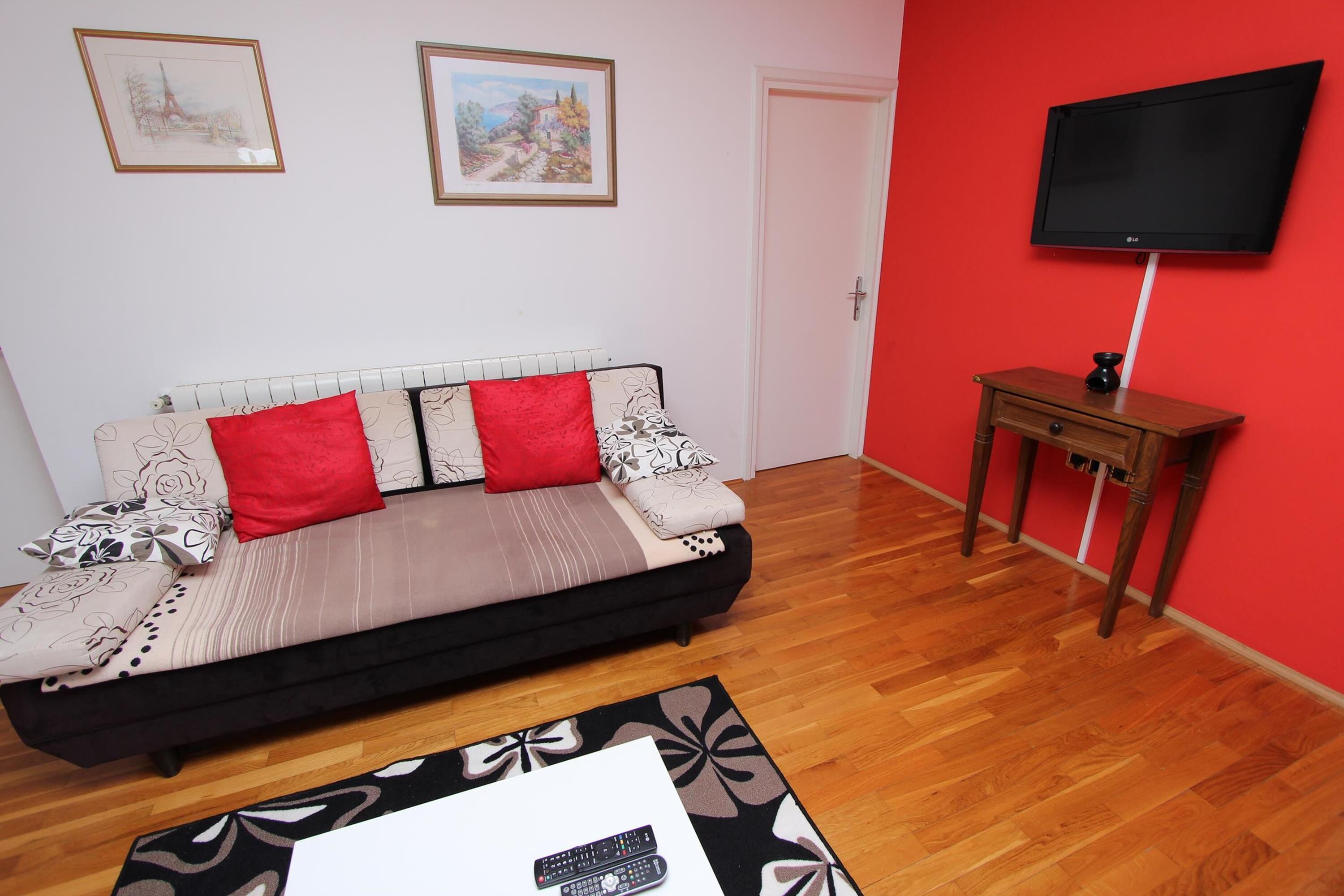 A living room with a sofa, a TV mounted on the wall, and a small wooden table.