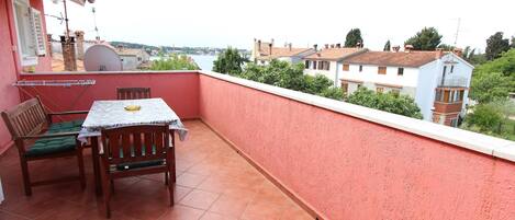 A balcony with a table and chairs, a red wall, and a view of buildings and trees.