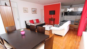 A living room with a sofa, a dining table with chairs, a kitchen area, and a red accent wall. - Apartment Suzana (Rovinj)