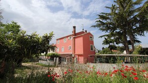 A two-story building with a red facade, surrounded by greenery and red flowers. - Apartment Suzana (Rovinj)