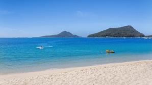 A beach with clear blue water, a sandy shore, and a mountain in the distance. - Seahaven 1 close to Shoal Bay Beach (Shoal Bay)