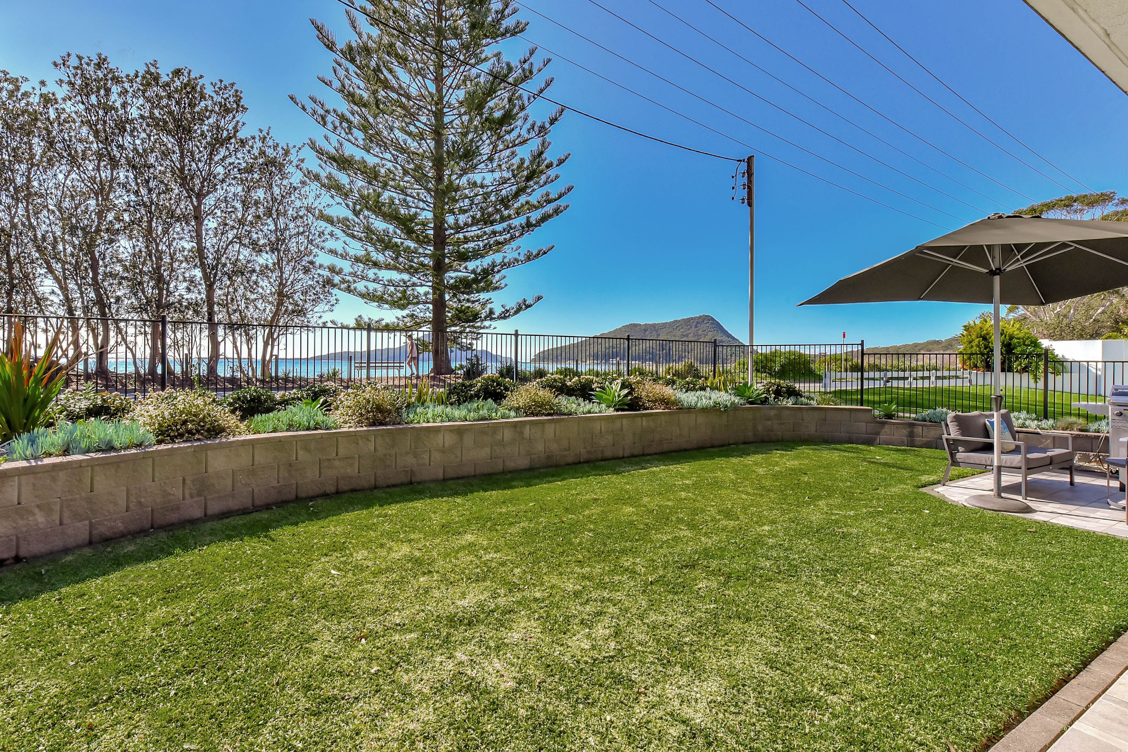 A well-maintained outdoor area with a grassy lawn, a seating area with a table and chairs, and a view of the sea.