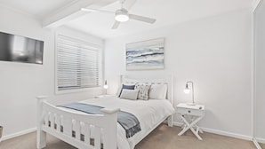 A bedroom with a white bed, a nightstand, a ceiling fan, a window with blinds, and a wall-mounted picture. - Seahaven 1 close to Shoal Bay Beach (Shoal Bay)