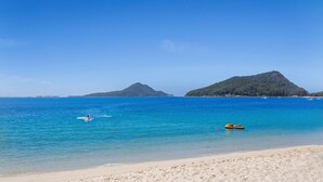 Une plage avec une eau d’un bleu limpide, un rivage sablonneux et deux collines en arrière-plan.