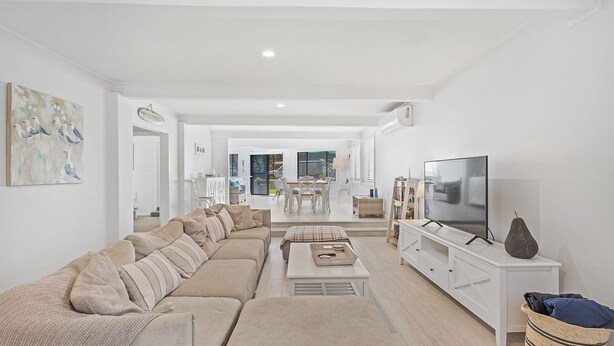 Un salon spacieux avec un grand canapé d’angle beige, un téléviseur à écran plat et un coin repas à l’arrière-plan.