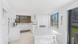 Une cuisine moderne avec des meubles blancs, un îlot central et une vue sur l’extérieur grâce à de grandes fenêtres.