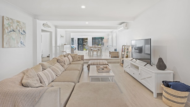A modern living room with a sectional sofa, a flat-screen TV, and a dining area in the background. - Seahaven 1 close to Shoal Bay Beach (Shoal Bay)