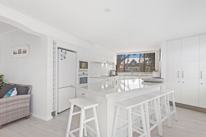 A modern kitchen with white cabinetry, a central island with bar stools, and a view through the window.