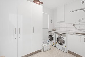 A modern laundry room with two front-loading washing machines, a drying rack, and a small laundry basket.
