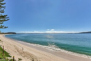 A beach with clear blue water, a sandy shore, and a distant shoreline.