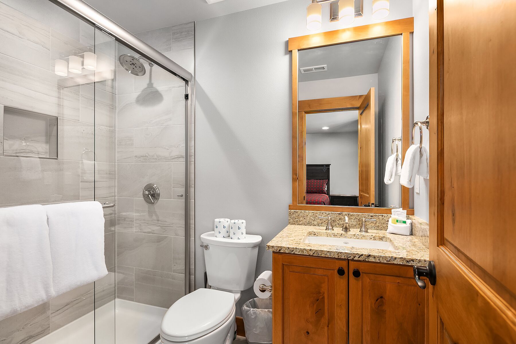 Un baño moderno con cabina de ducha de vidrio, inodoro, lavabo con tocador y espejo.