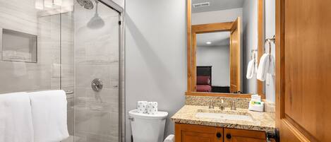 Un baño moderno con cabina de ducha de vidrio, inodoro, lavabo con tocador y espejo.