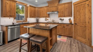 Una cocina moderna con armarios de madera, lavavajillas de acero inoxidable y una isla central con taburetes.