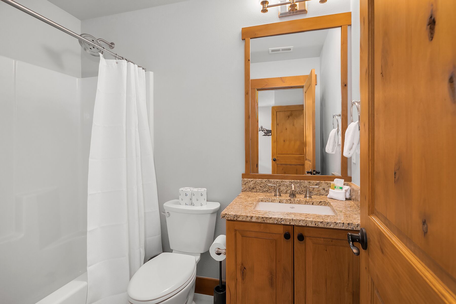 Een badkamer met een wit toilet, een wastafel met een granieten blad, een houten kastje en een spiegel boven de wastafel.