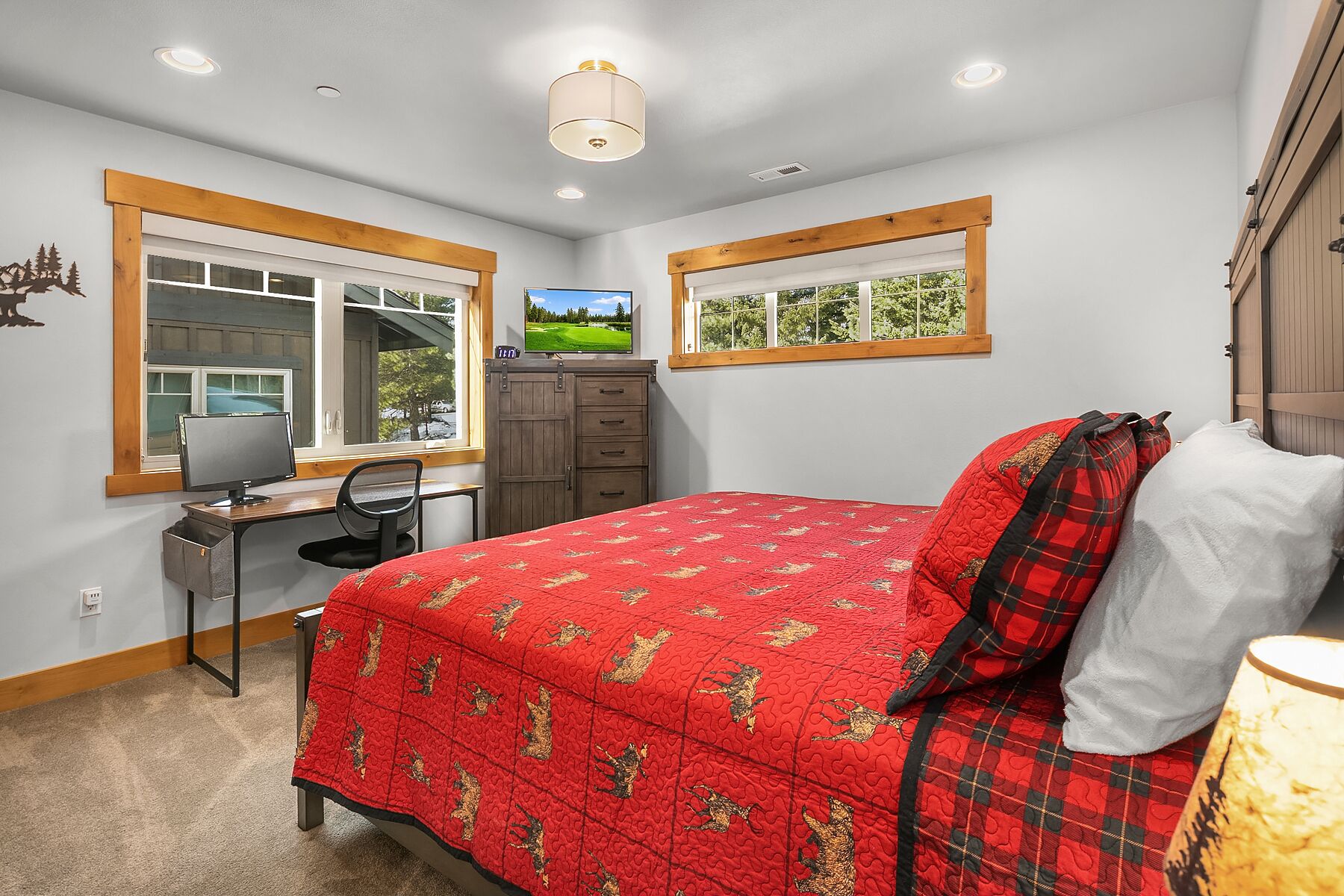 A bedroom with a bed, desk, chair, and two windows.