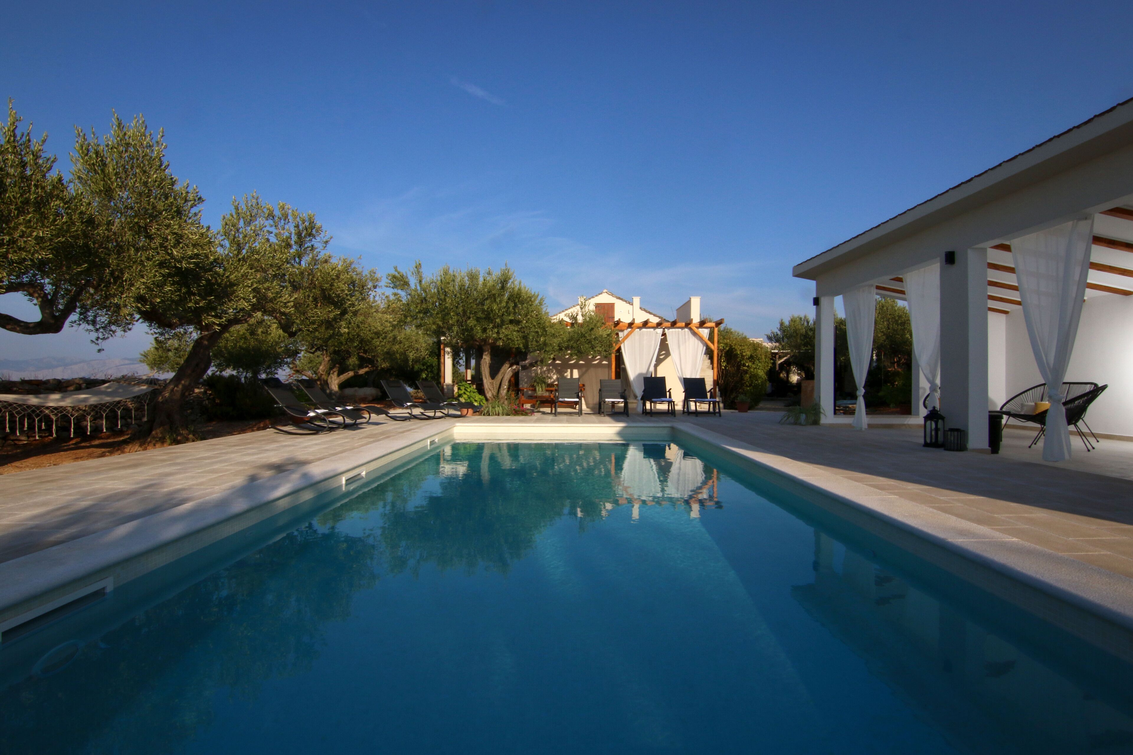 A swimming pool with lounge chairs and a pergola with white curtains.