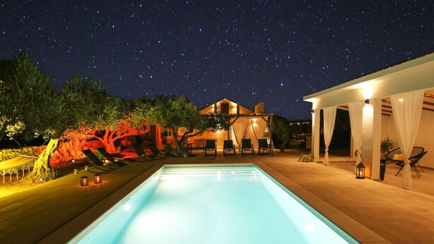Una piscina con vistas a una casa y árboles de noche.