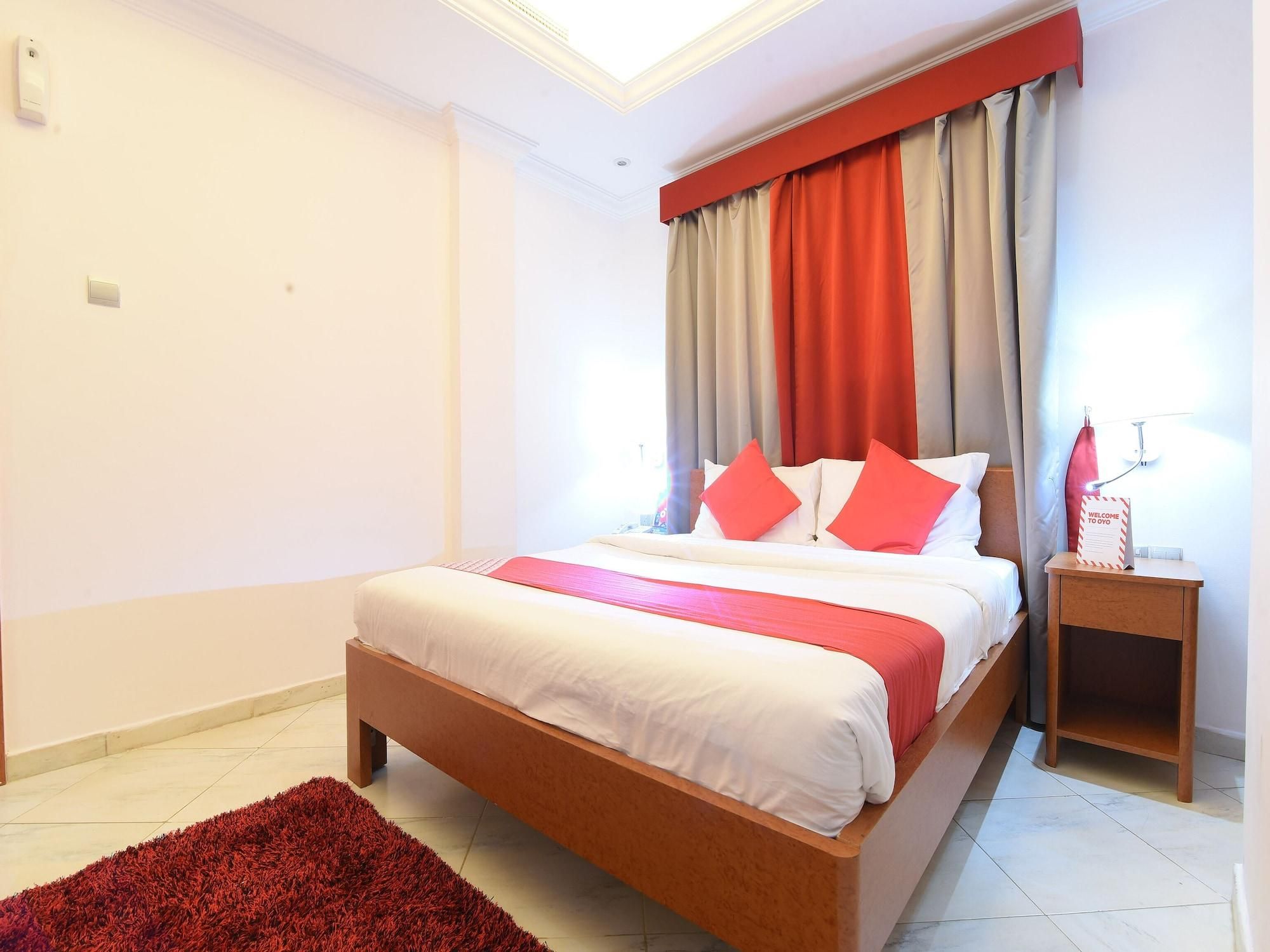 A bedroom with a bed, a nightstand, a red rug, and a ceiling light.