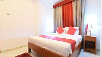 Un dormitorio con una cama, una mesita de noche, una alfombra roja y una lámpara de techo.