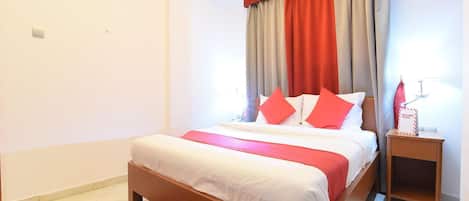 A bedroom with a bed, a nightstand, a red rug, and a ceiling light.