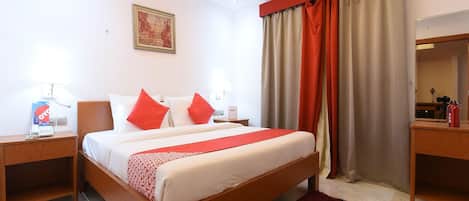 A hotel room with a bed, two bedside tables, a red throw, a red rug, a painting on the wall, and a window with curtains.