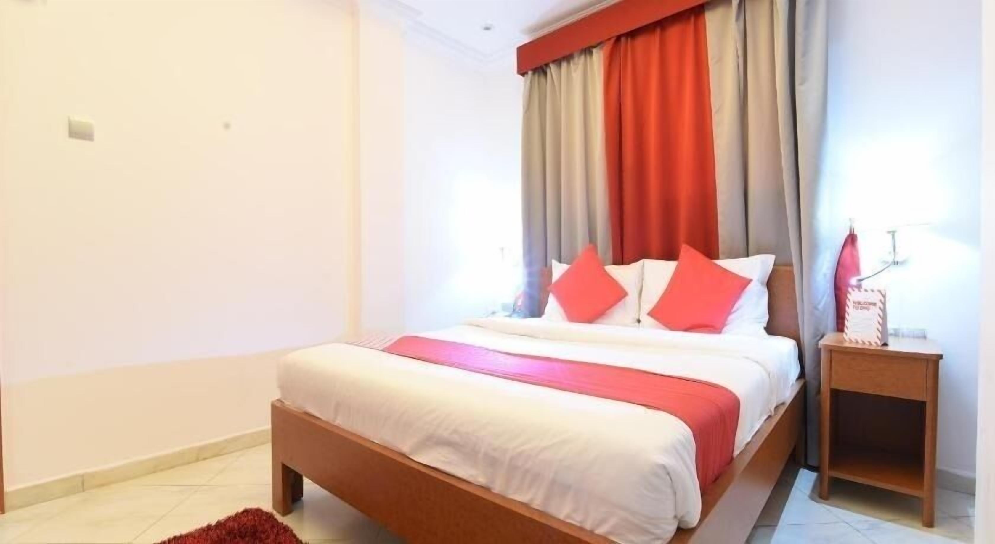 A bedroom with a bed, curtains, a nightstand, and a red rug.