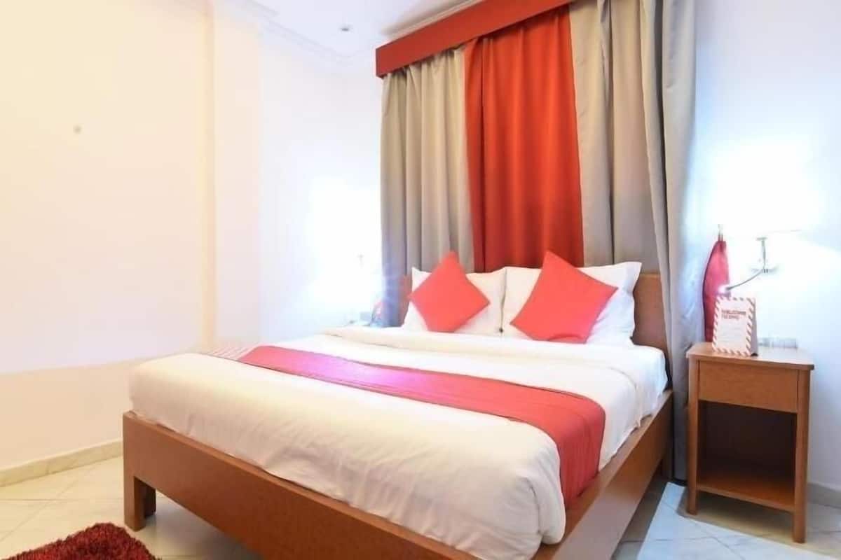 A bedroom with a bed, curtains, a nightstand, and a red rug.