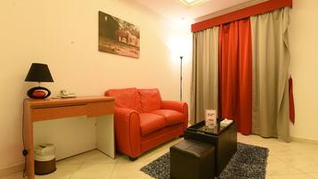 A compact living space with a sofa, a desk, a lamp, and a painting on the wall.