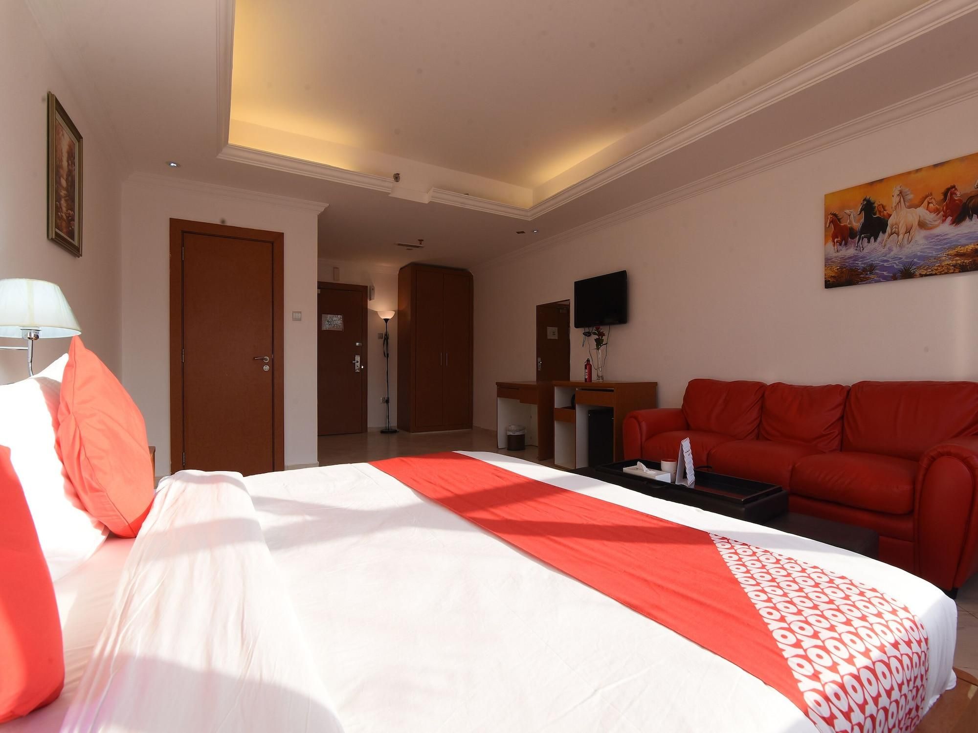 A hotel room with a bed, a red sofa, a flat-screen TV, and a painting on the wall.