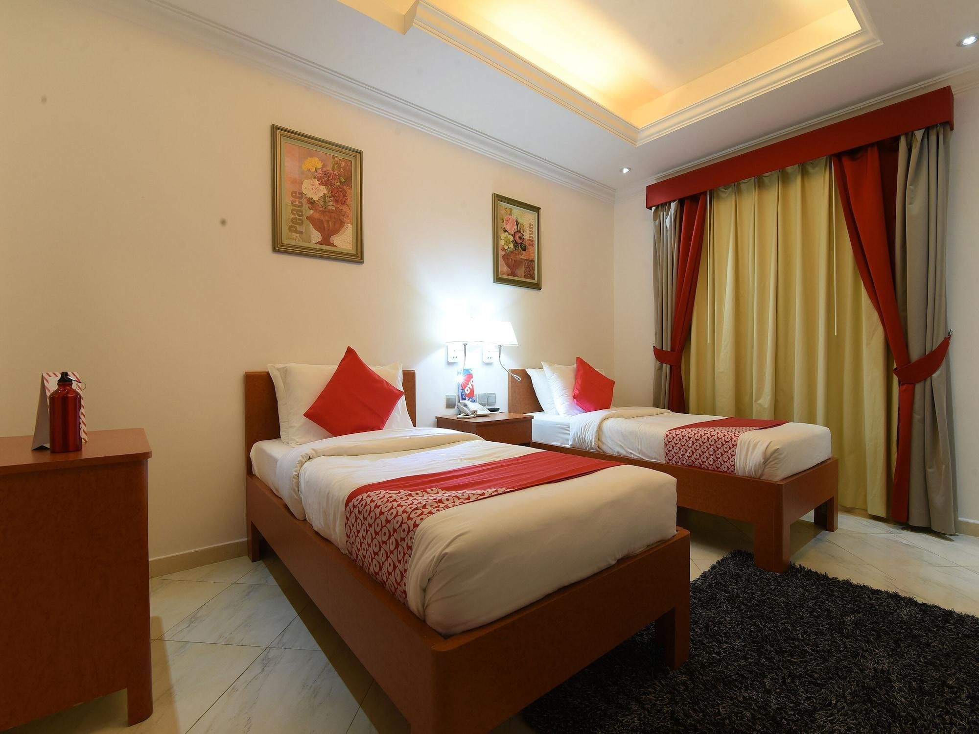 A hotel room with two beds, a desk, a nightstand, a lamp, and a window with curtains.