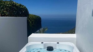 Ein Whirlpool mit Bedienfeld, umgeben von einer weißen Mauer, mit Blick auf den Ozean und einem grünen Hecken im Hintergrund.