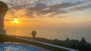 Ein Swimmingpool mit Sonnenuntergangsblick, eine Lounge und ein klarer Himmel.