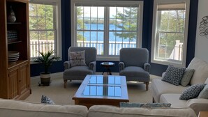 Een woonkamer met een grote erker, een bank, twee fauteuils, een salontafel en een houten kast met decoratieve objecten.