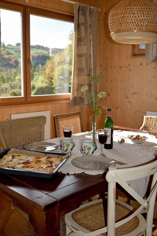 A dining table set with a pizza, wine, and glasses, overlooking a scenic view.
