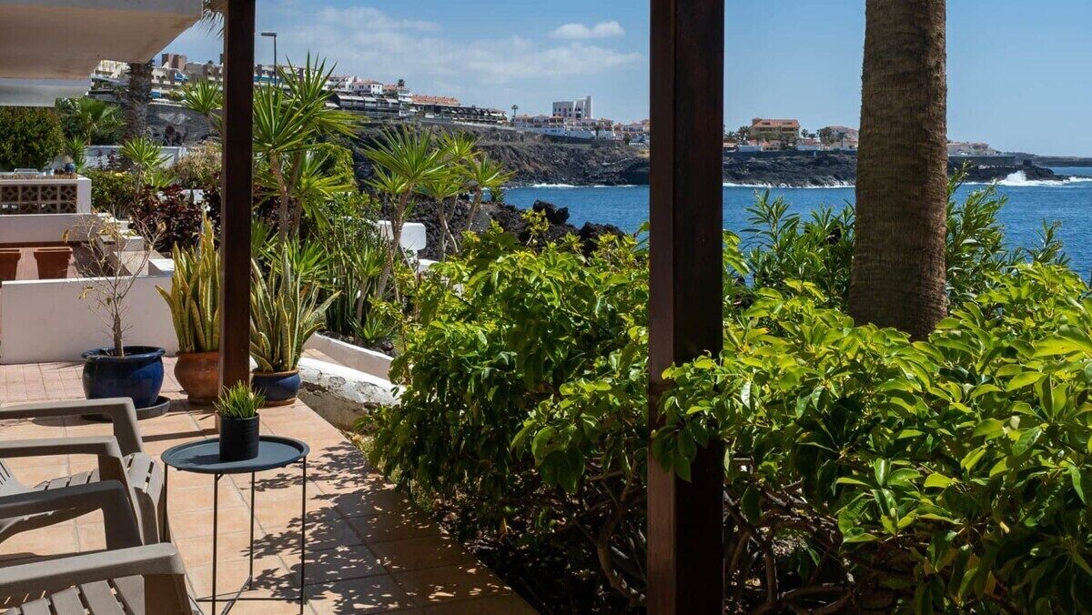 Une terrasse agrémentée de plantes en pot, de mobilier d’extérieur et offrant une vue sur la mer et les bâtiments qui se dressent à l’arrière-plan.