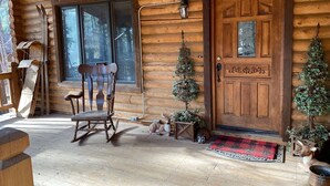 A wooden cabin with a wooden porch, a rocking chair, a small Christmas tree, and a deer statue. - Private Mountain True Log Cabin Retreat with 2 Master Bedrooms (Strawberry)