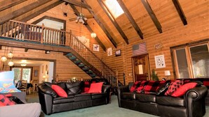 A log cabin interior with a loft bedroom, a dining area, and a living room with leather sofas and red cushions. - Private Mountain True Log Cabin Retreat with 2 Master Bedrooms (Strawberry)