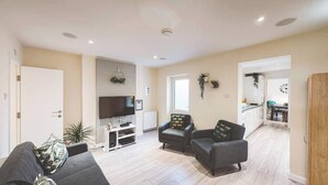 A modern living room with a flat-screen TV, two sofas, a coffee table, and a small TV stand. - Perfect for contractors, 4-bedrooms, sleeps 7! (Crewe)