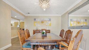 Ein Esszimmer mit einem großen Holztisch, der von sechs Stühlen umgeben ist, einer Chandelierleuchtre und floralen Bildern an den Wänden.