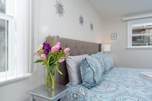 Ein Schlafzimmer mit einem Bett, einem Nachttisch, einer Vase mit Blumen und dekorativen Wandspiegeln.