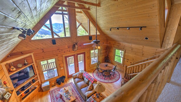 A wooden cabin interior with a loft bedroom, a living area with a sofa and TV, and a dining area with a table and chairs. - Spectacular Views, Privacy and Hot Tub (Maggie Valley)
