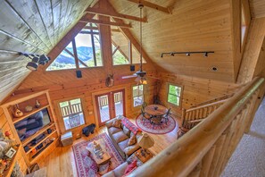 L’intérieur d’un chalet en bois comprend une chambre à coucher située en mezzanine, un espace de vie avec un canapé et une télévision, ainsi qu’un coin repas avec une table et des chaises.