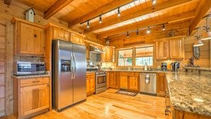 A spacious kitchen with wooden cabinets, stainless steel appliances, granite countertops, and a large window providing natural light. - Spectacular Views, Privacy and Hot Tub (Maggie Valley)
