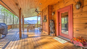 A wooden deck with a covered area, a red door, and a bear statue. - Spectacular Views, Privacy and Hot Tub (Maggie Valley)